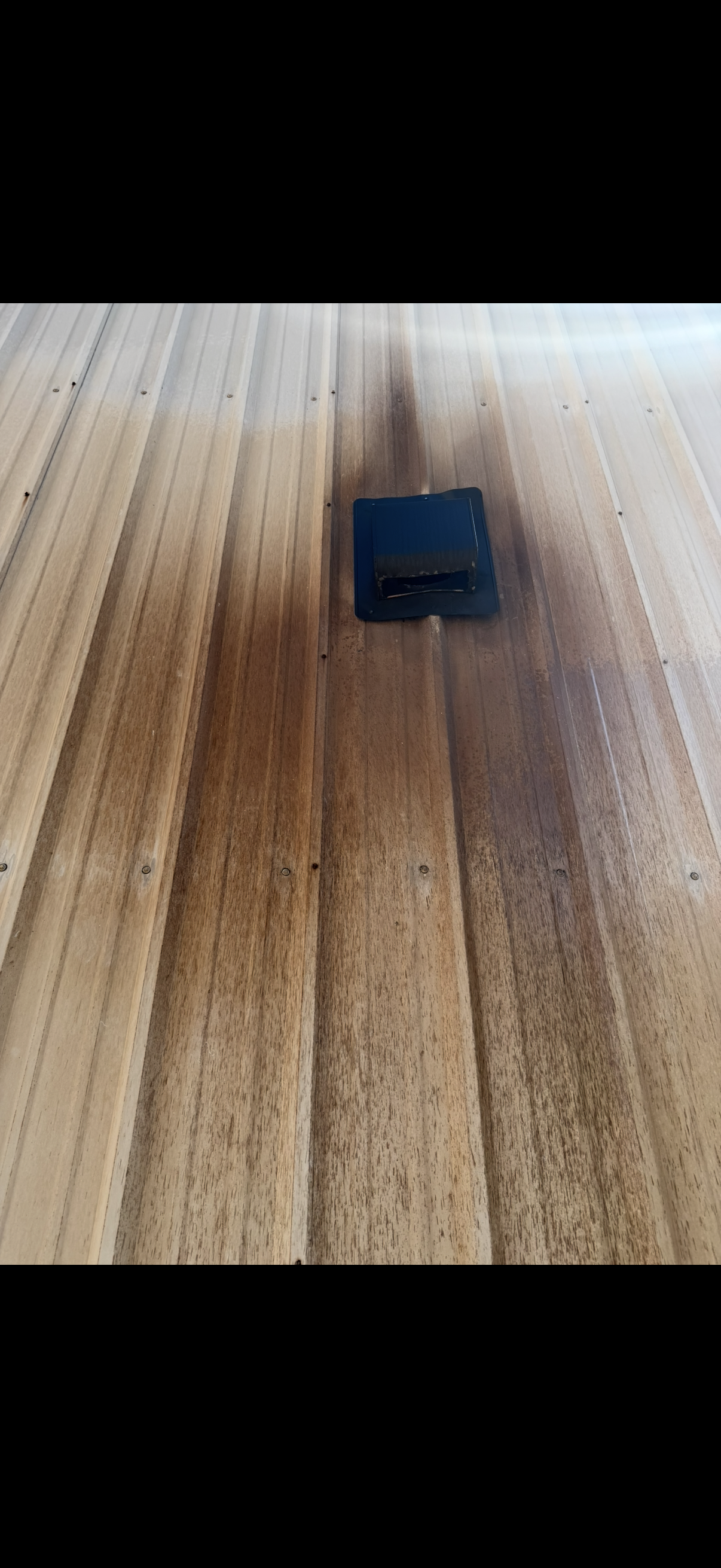 A small black square object resting on a wooden surface with a charred, scorched burn mark radiating outward from it.
