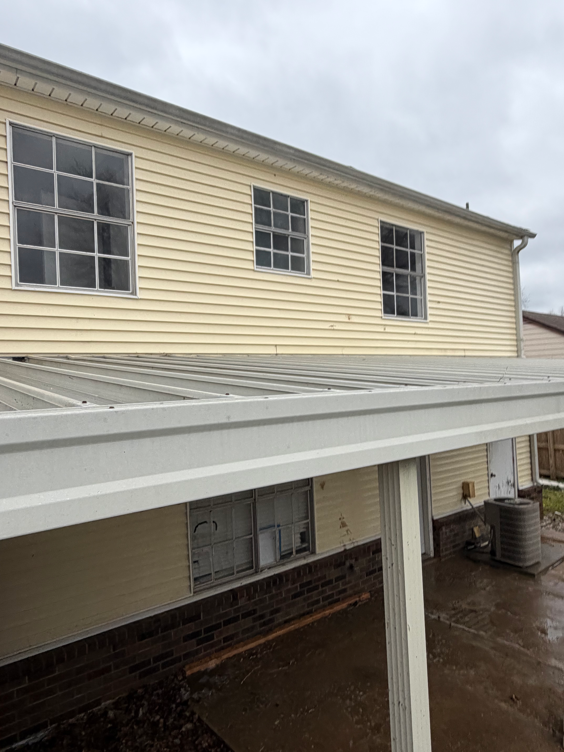 A two-story building exterior with yellow siding, a white metal patio cover, and stone accents along the foundation.
