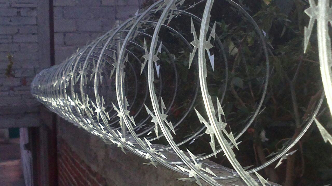 Un primer plano de una valla de alambre de púas con una pared de ladrillos al fondo.
