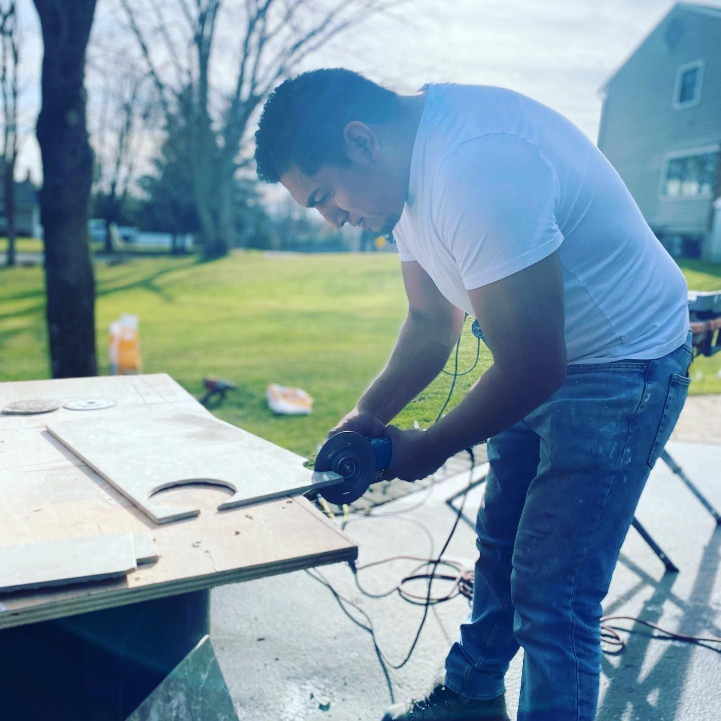 Man in jeans and a white shirt using a saw outdoors to cut wood.