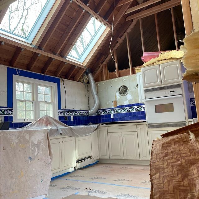 Kitchen under renovation, exposed wood beams, cabinets, blue tile backsplash, skylights, and windows.