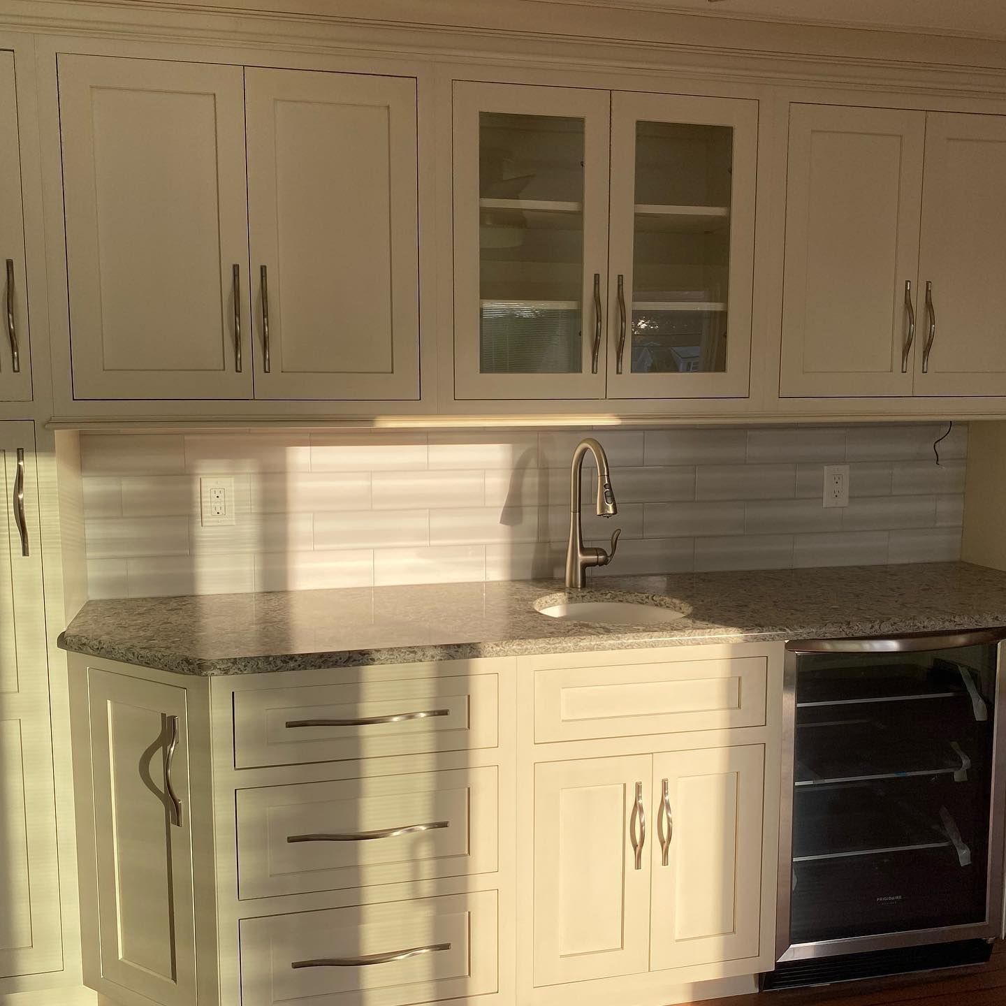White kitchen cabinets with a granite countertop, sink, and wine cooler.