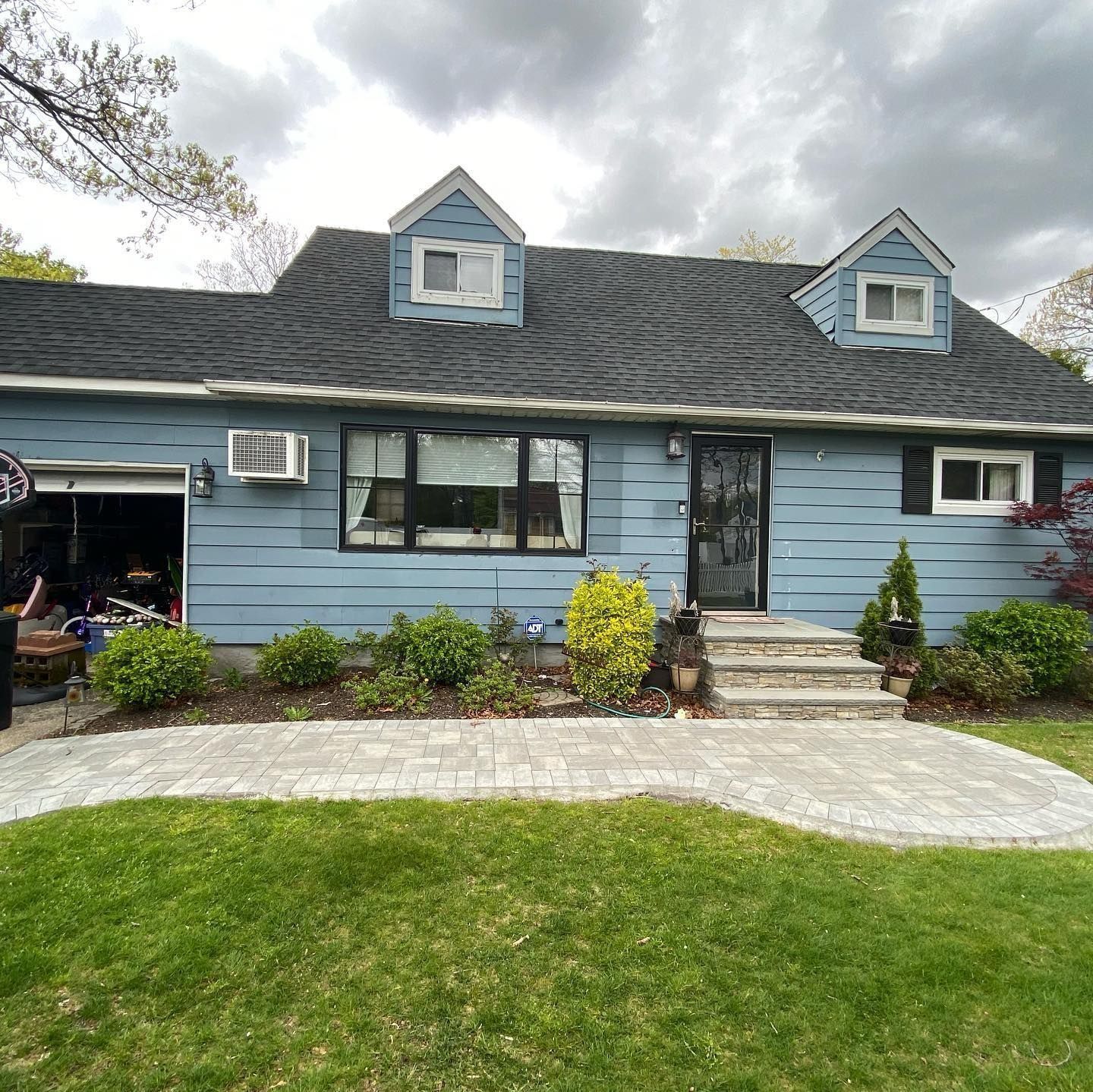 Blue house with black roof, two dormers, landscaping, and paved walkway.