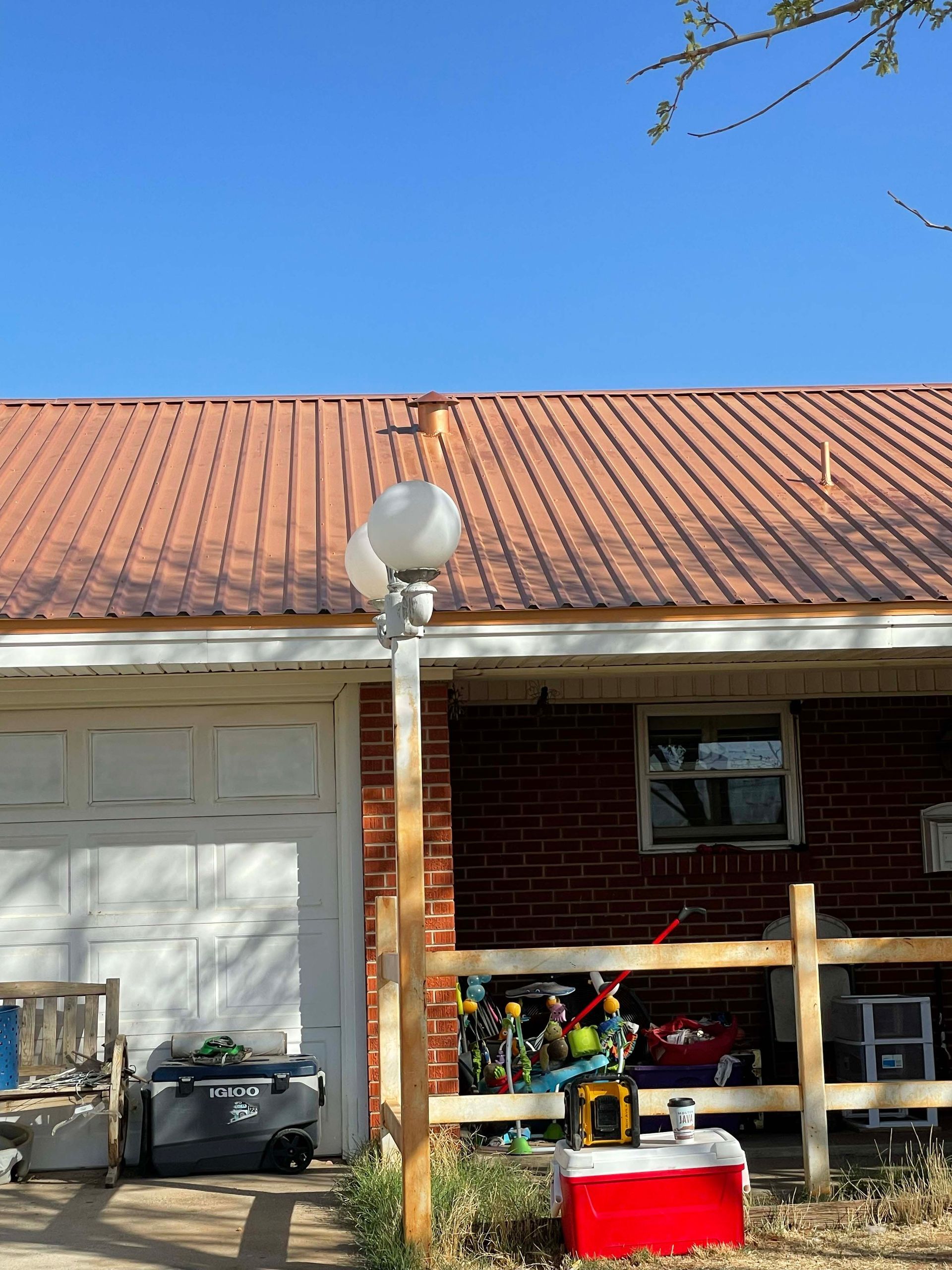A brick house with a brown metal roof, white garage door, and a street lamp in front.