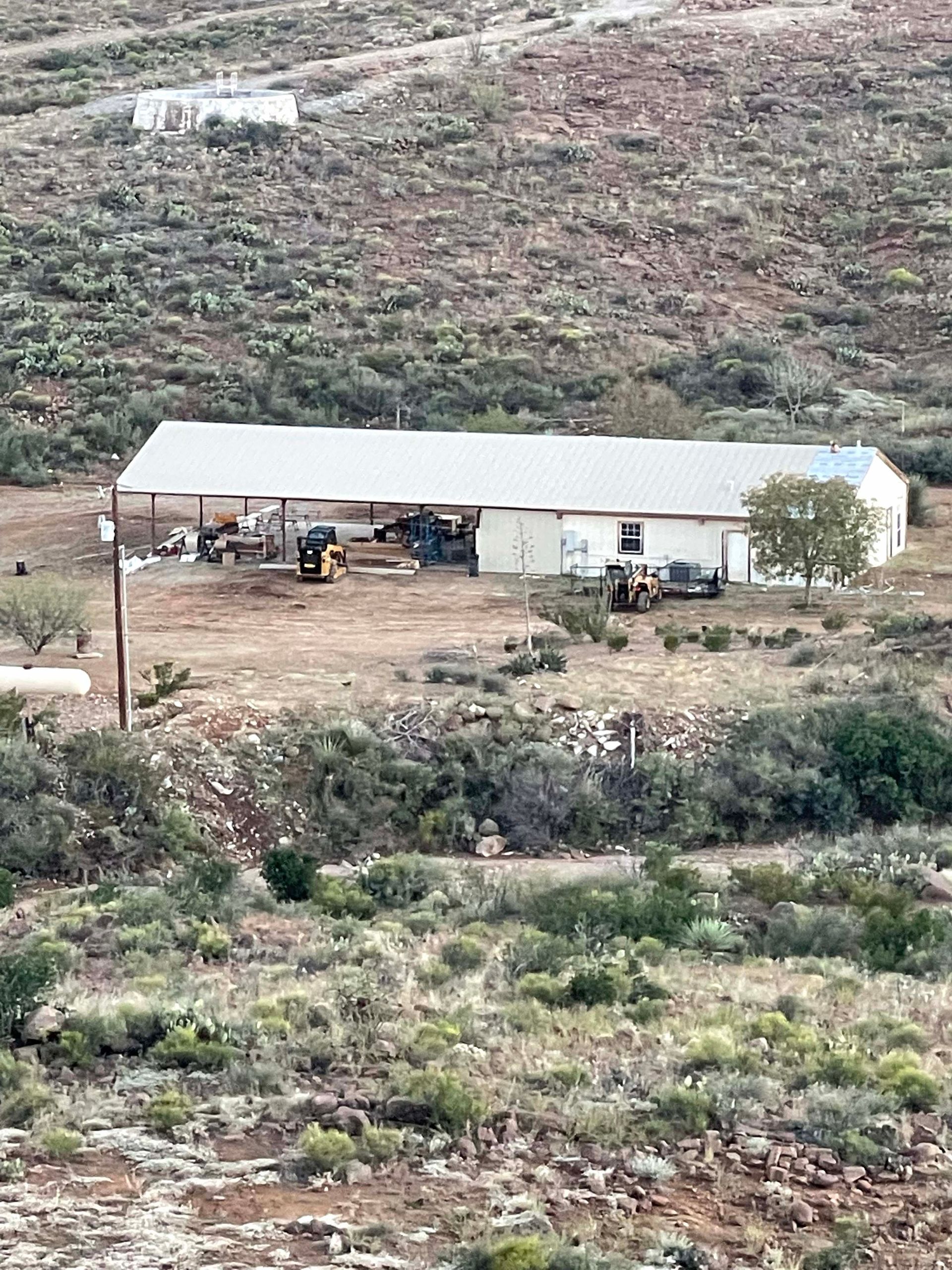 A single-story white building with a metal roof in a desert landscape; two tractors outside.
