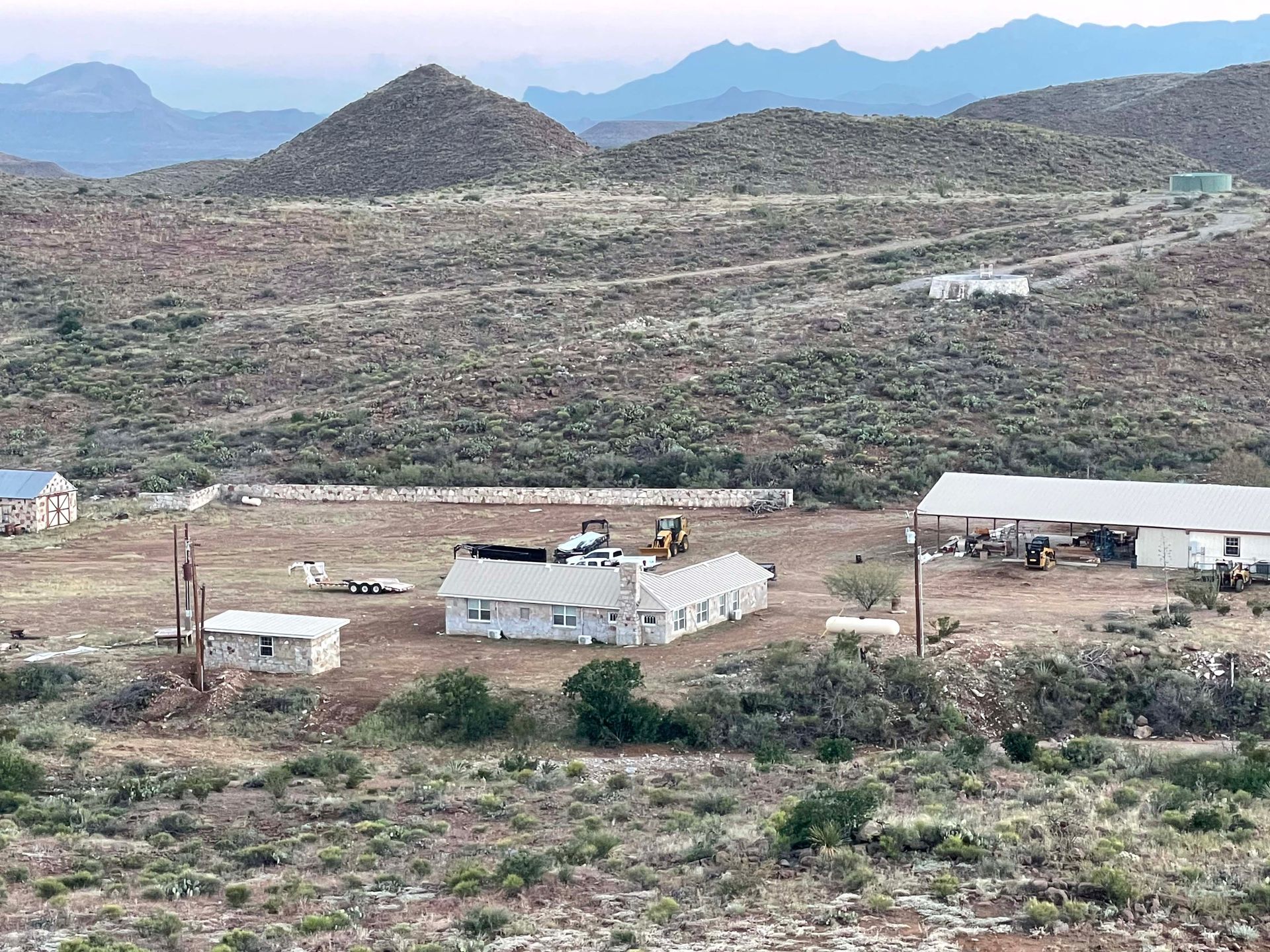 Rural landscape with buildings, including a large white structure and surrounding low hills with sparse vegetation.