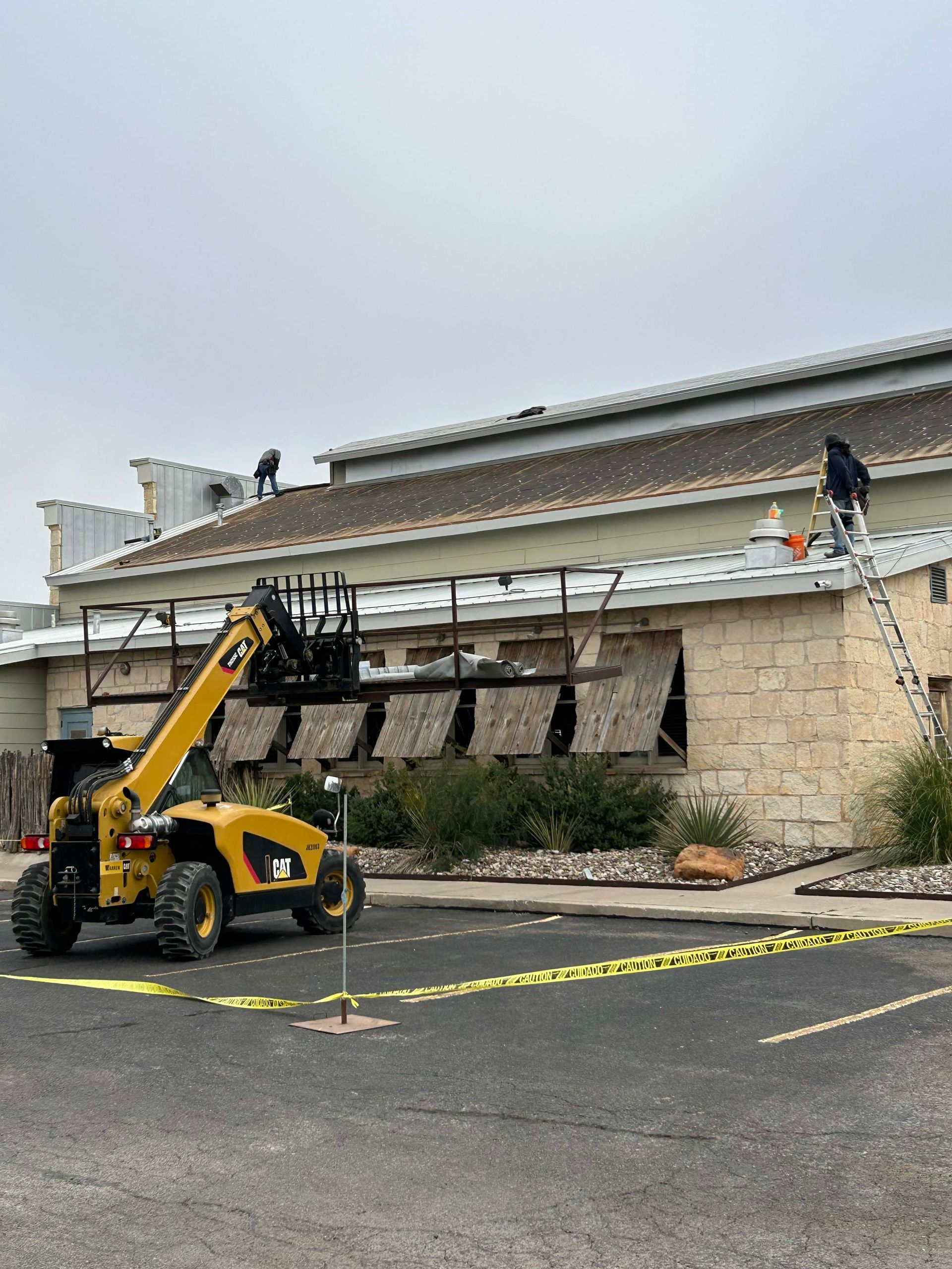 Yellow forklift near building with workers on roof.  Construction scene, safety tape present.