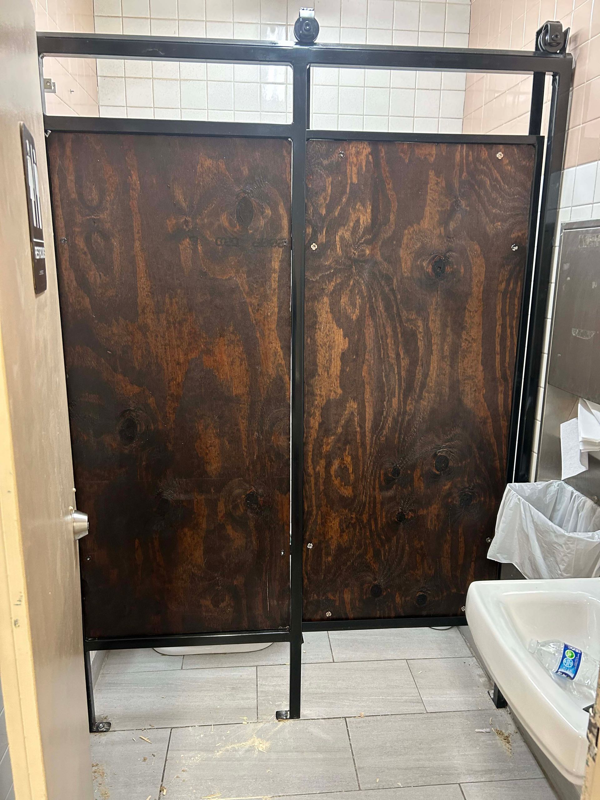 Dark wood restroom stall doors with black metal frame; public bathroom.