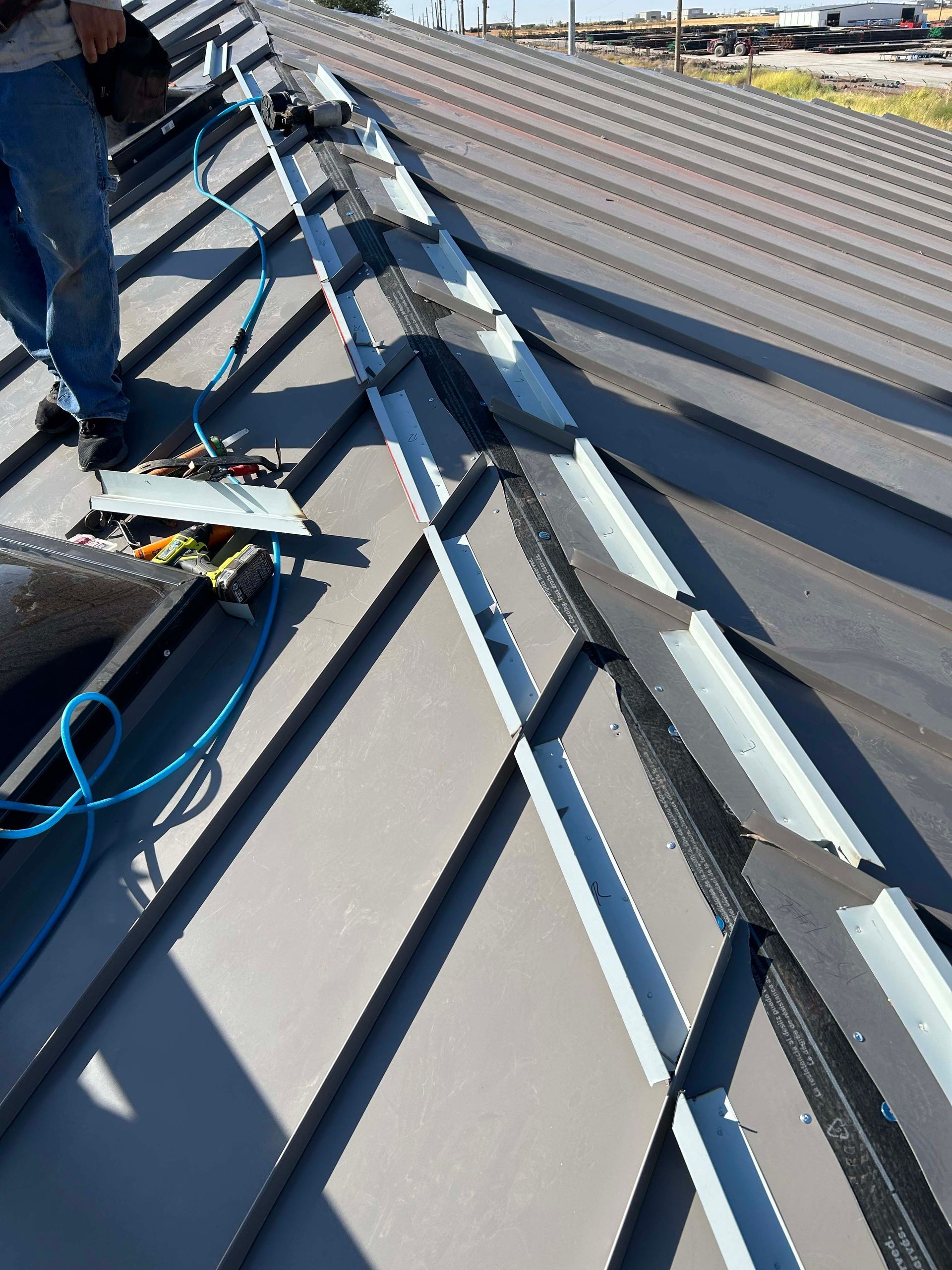 Person working on a gray metal roof, possibly installing or repairing flashing.