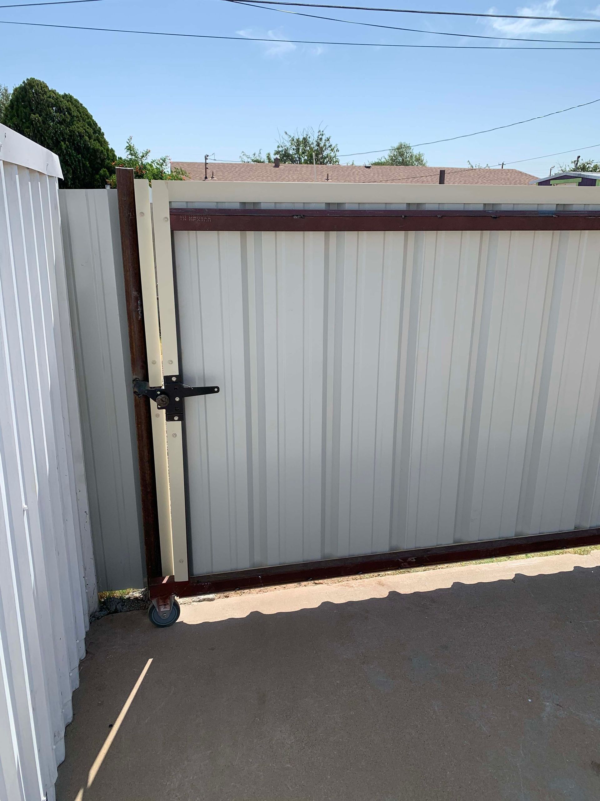 Metal gate with vertical panels and brown trim, attached to a fence.