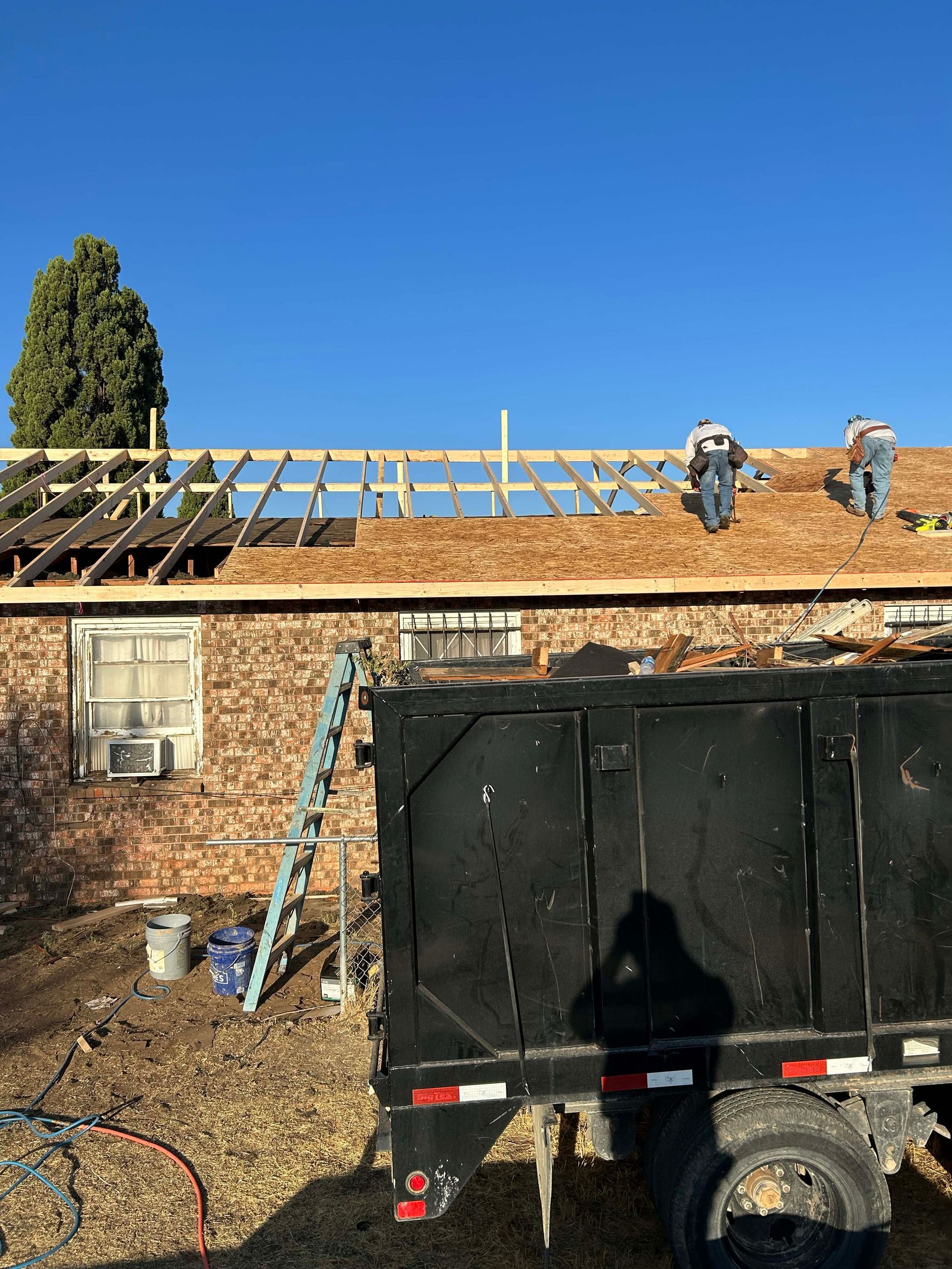 Roofing crew working on a house; dump truck, ladder, and tools are on site.