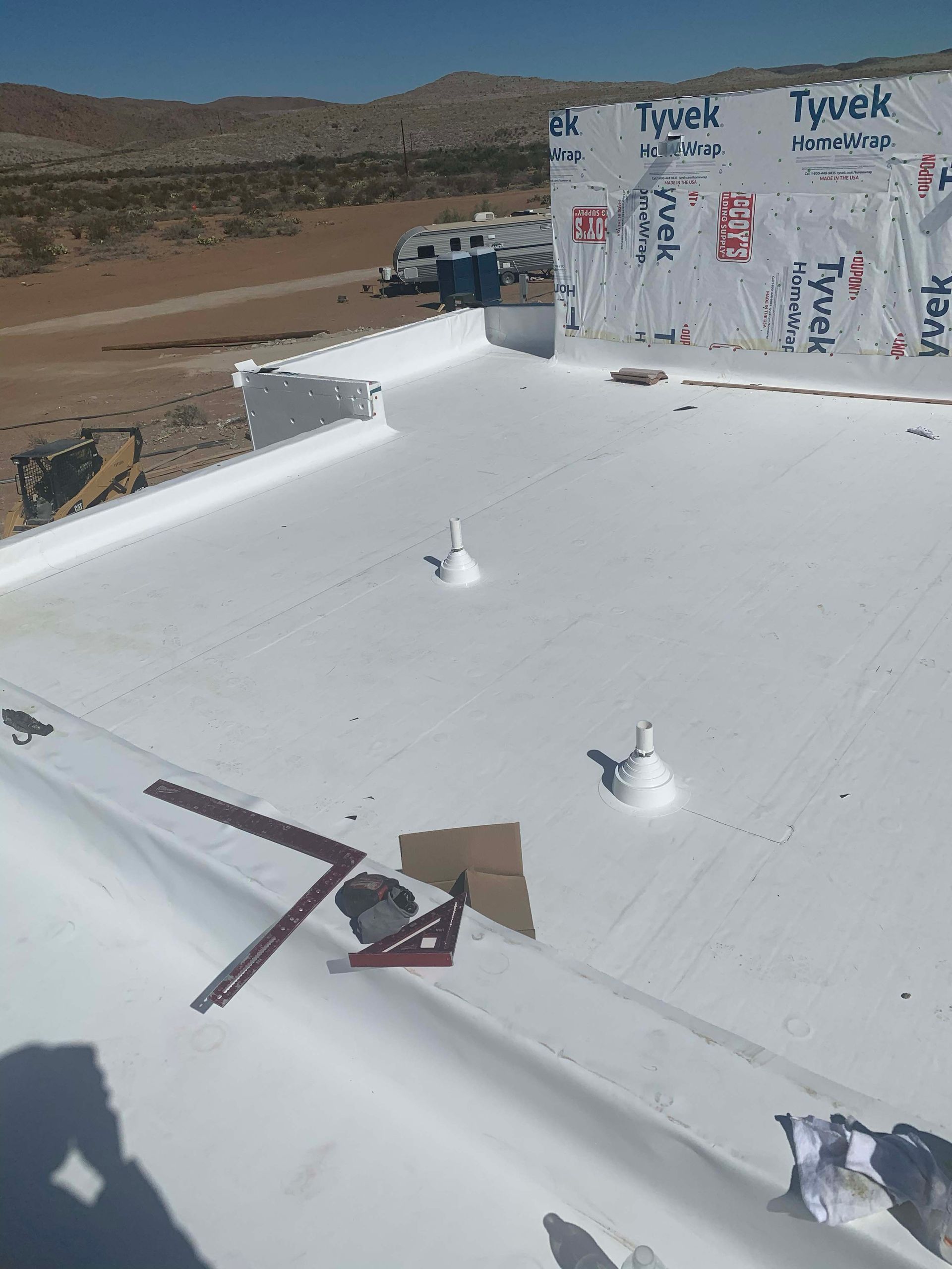 White flat roof with vents and construction materials, set in a desert landscape with distant mountains.