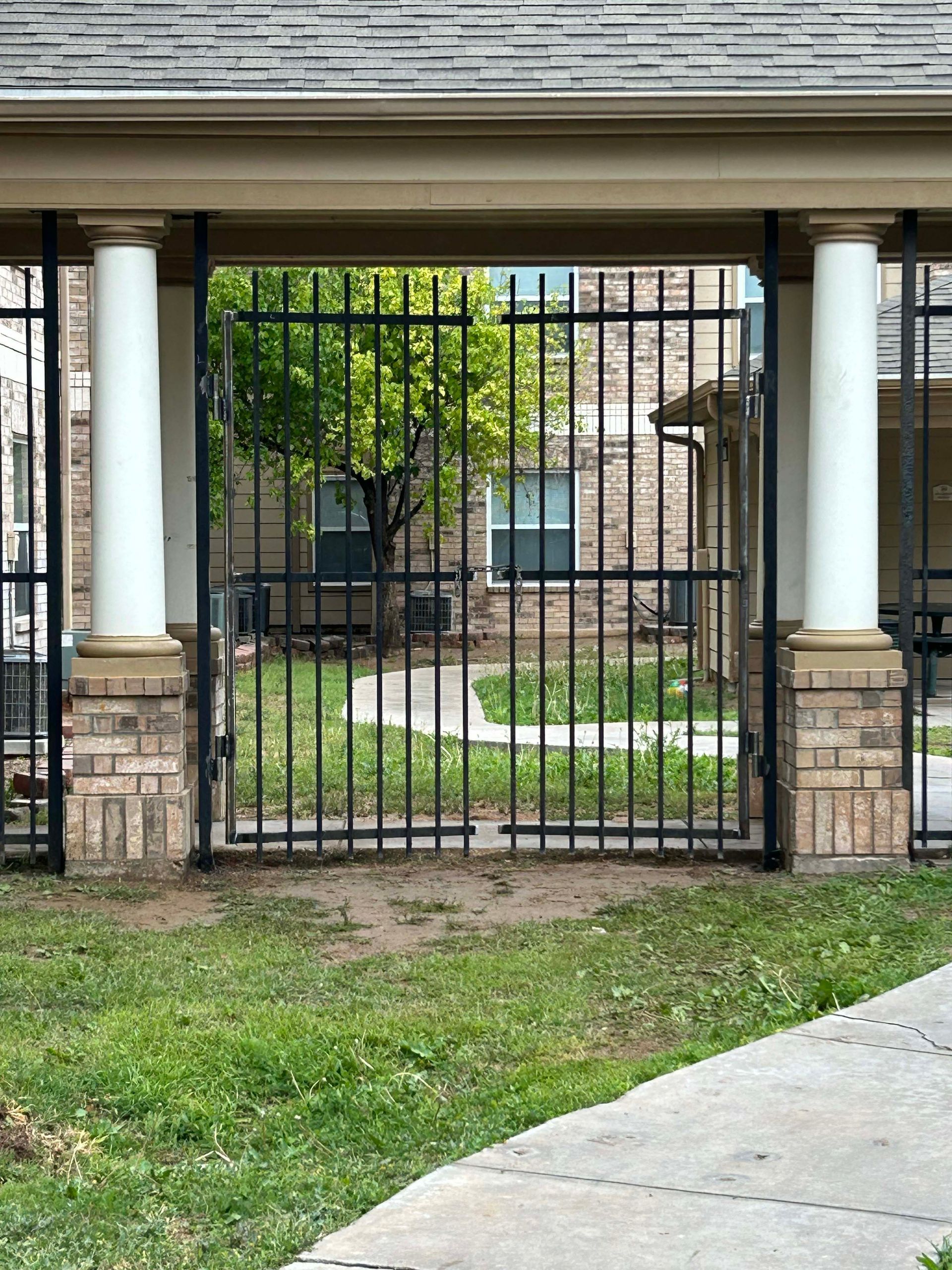 Black metal gate between brick and white pillars in a residential area.