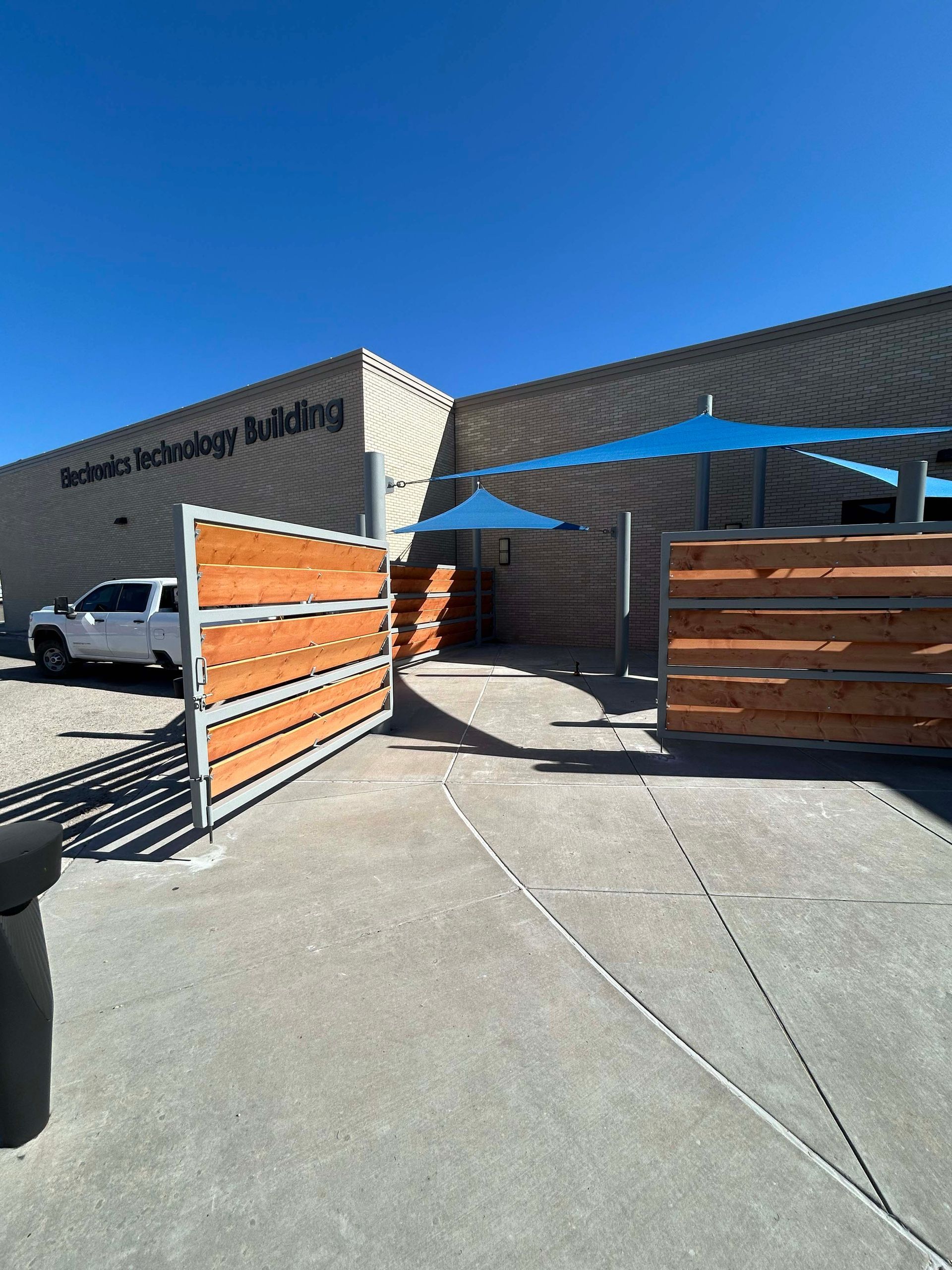 Exterior of the Renewable Technology Building with wooden fence, blue shade, and white truck under a clear sky.