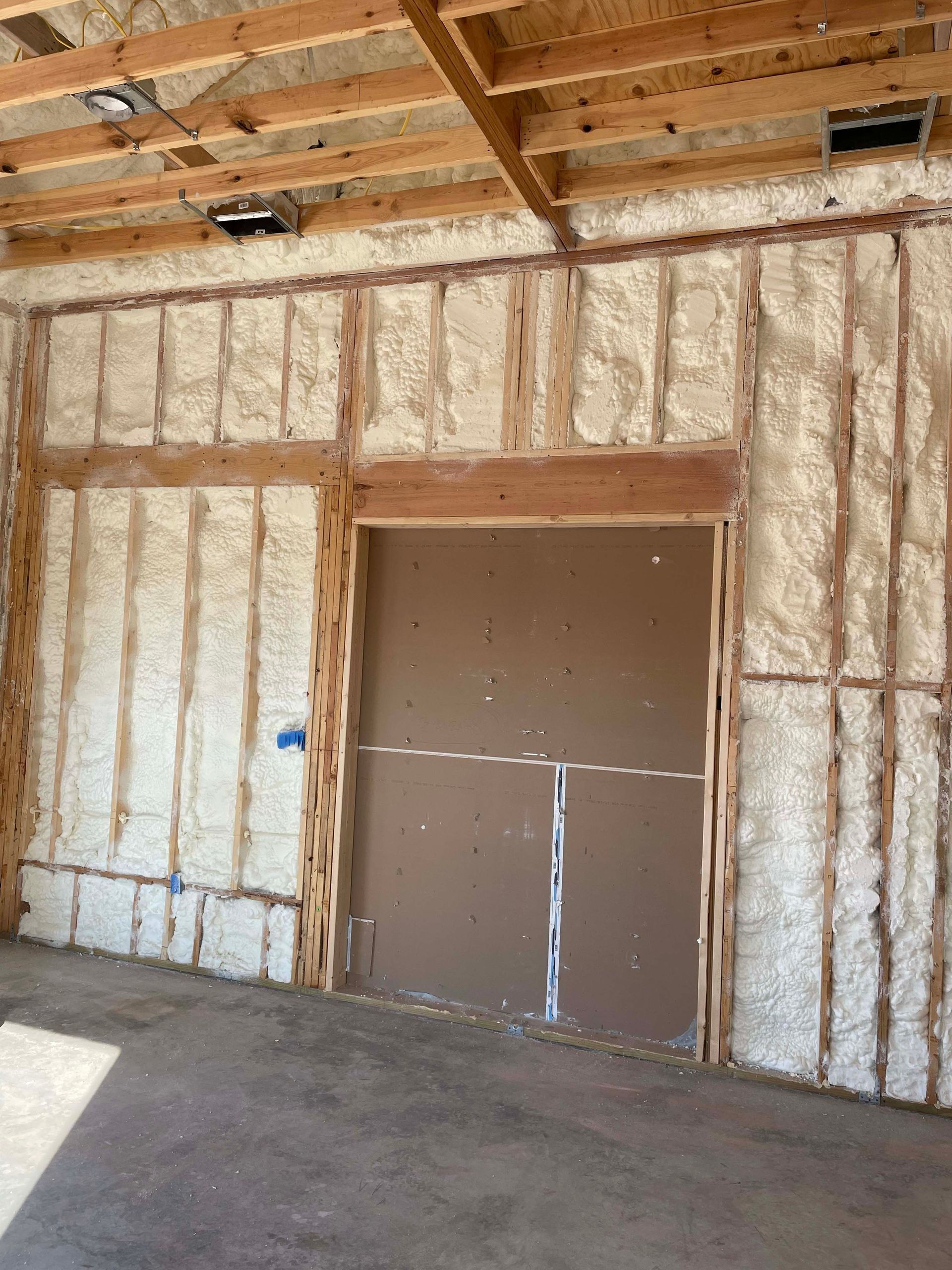 Interior view of a room with spray foam insulation on the walls and ceiling, surrounding a doorway.