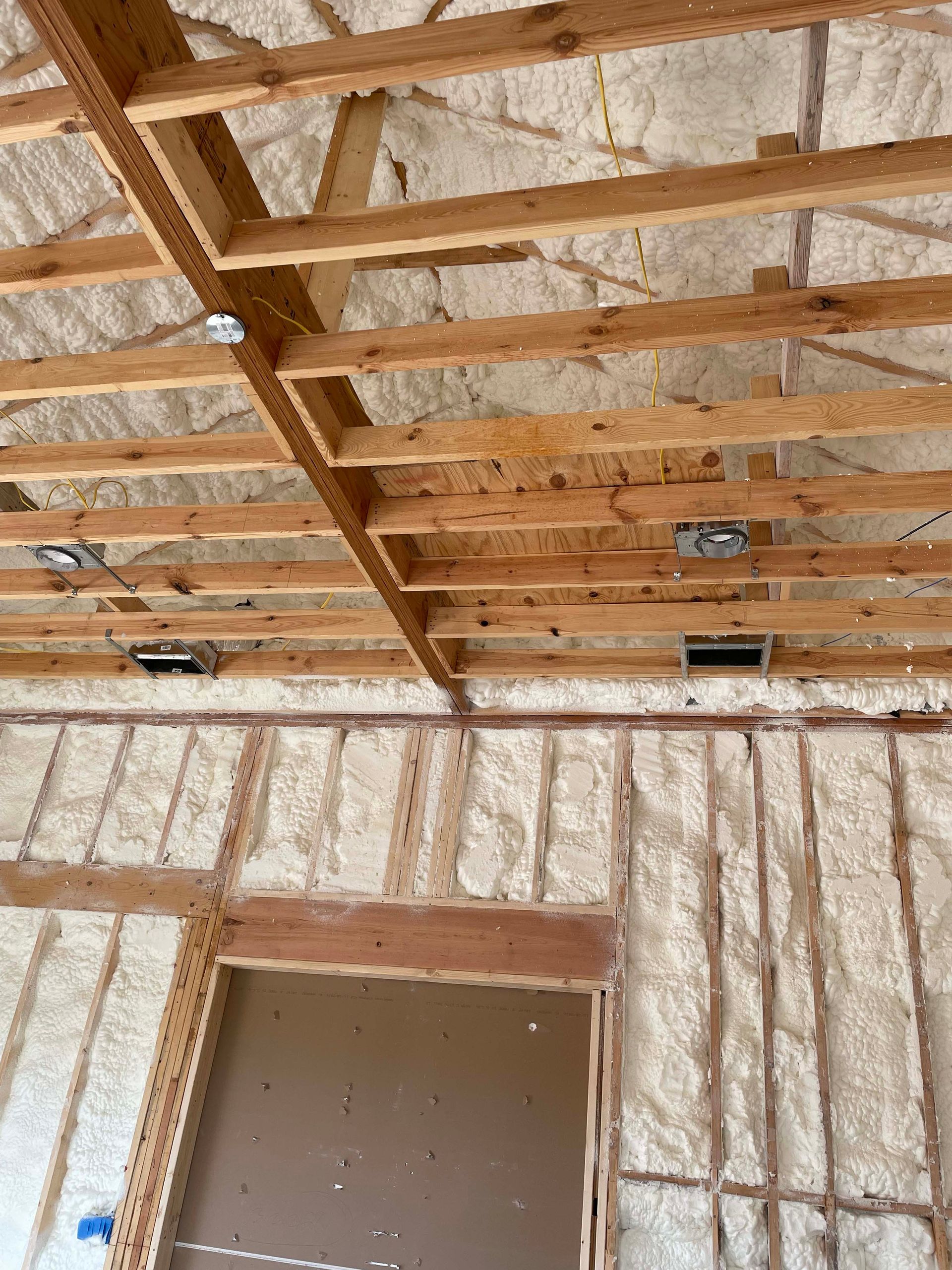 Interior view of a building under construction, showing wooden framing and spray foam insulation on walls and ceiling.