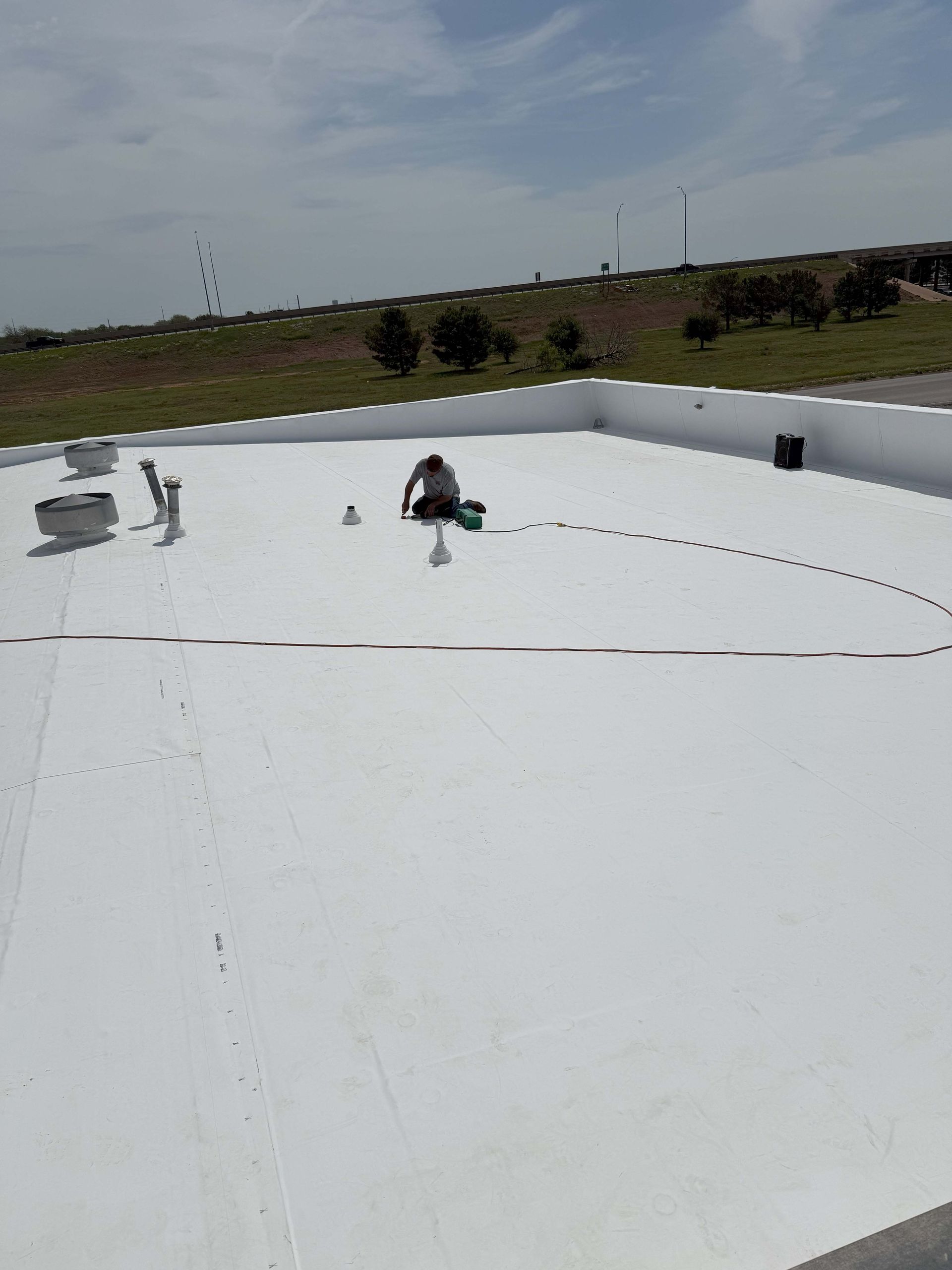 Person on a white flat roof, possibly repairing, under a blue sky.