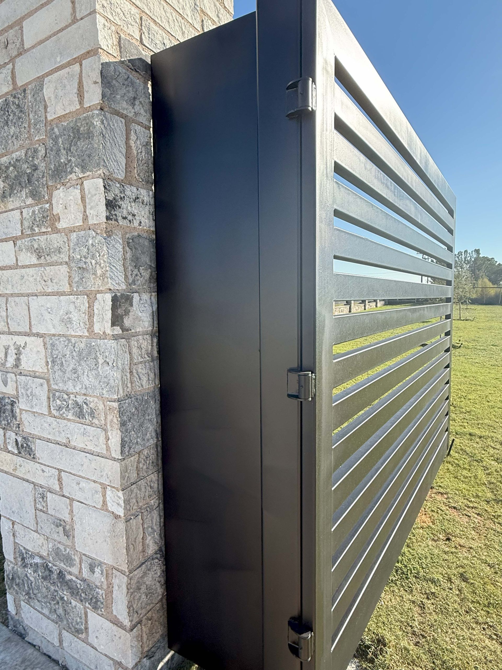 Black metal gate opening near a brick column; outdoors on grass.