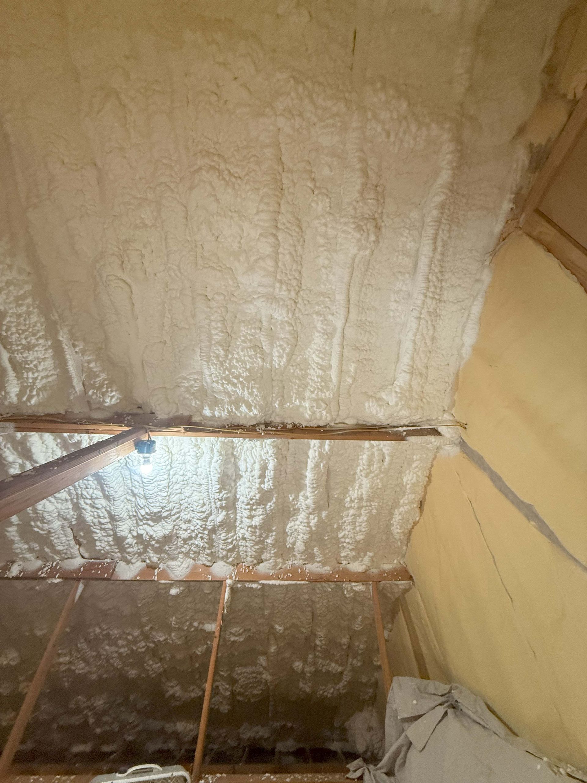 Attic ceiling insulated with spray foam; wooden beams and walls visible.