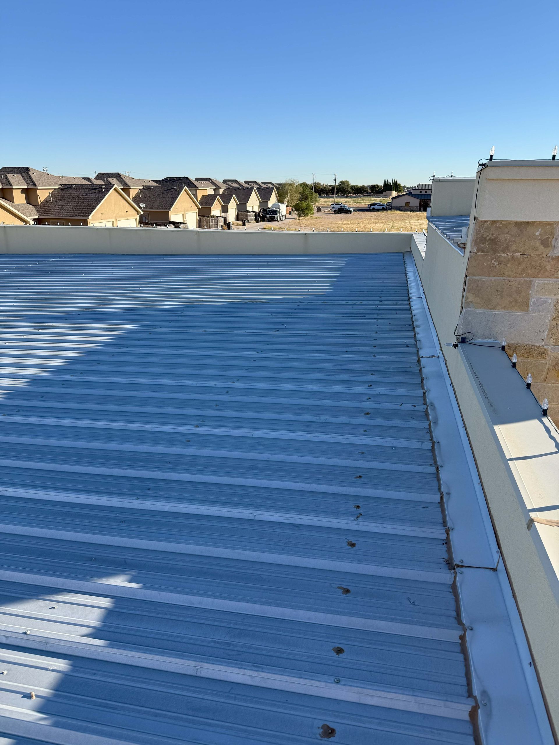 Flat metal roof with a white edge, overlooking a neighborhood under a blue sky.
