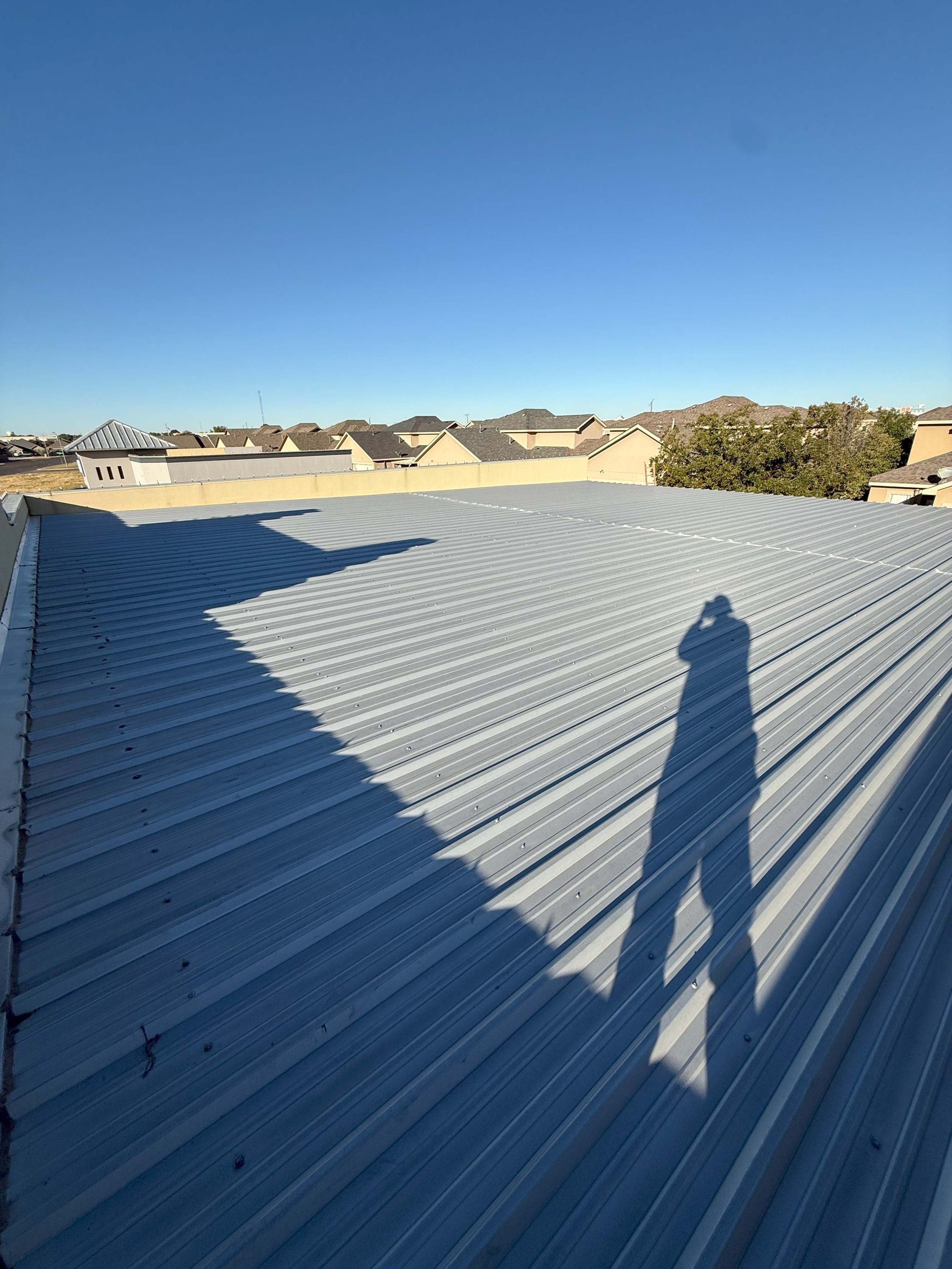 Metal roof under a clear blue sky, with a shadow of a person. Houses in the background.