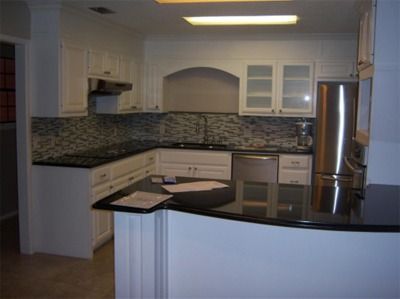 White kitchen with black countertops and stainless steel appliances.