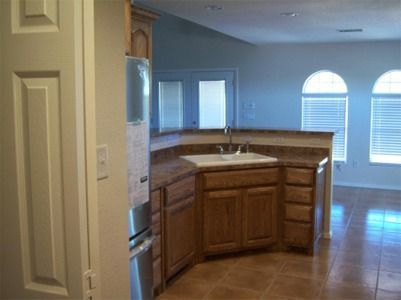Kitchen with wooden cabinets, sink, and countertop, open to living area with arched windows.