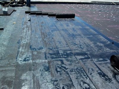 A flat roof being worked on, with large, black rolled roofing material.