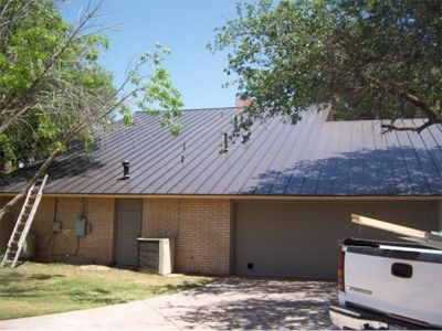 Brown metal roof on a single-story brick house with a white truck and a ladder leaning against the roof.