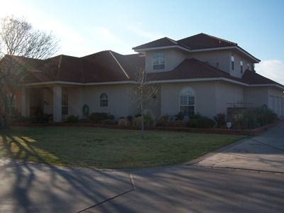 Large, tan house with red roof, grassy lawn, and driveway.