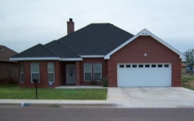 Red brick house with a dark roof and white garage door.