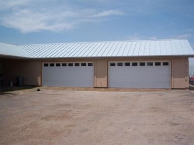 Two white garage doors under a light-colored metal roof on a building with a light-brown facade.