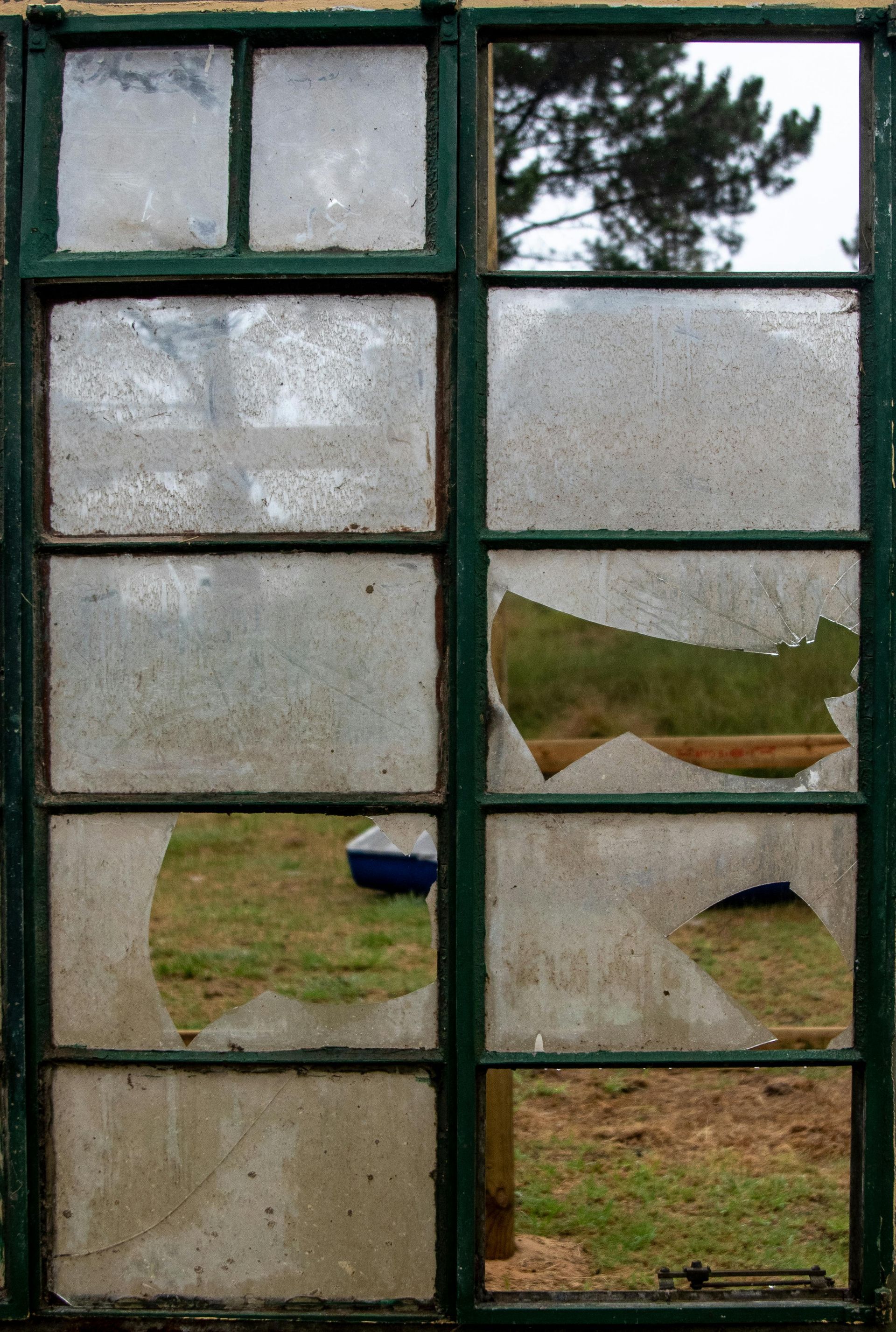 A weathered green window, partially broken, with a blurry outdoor view.