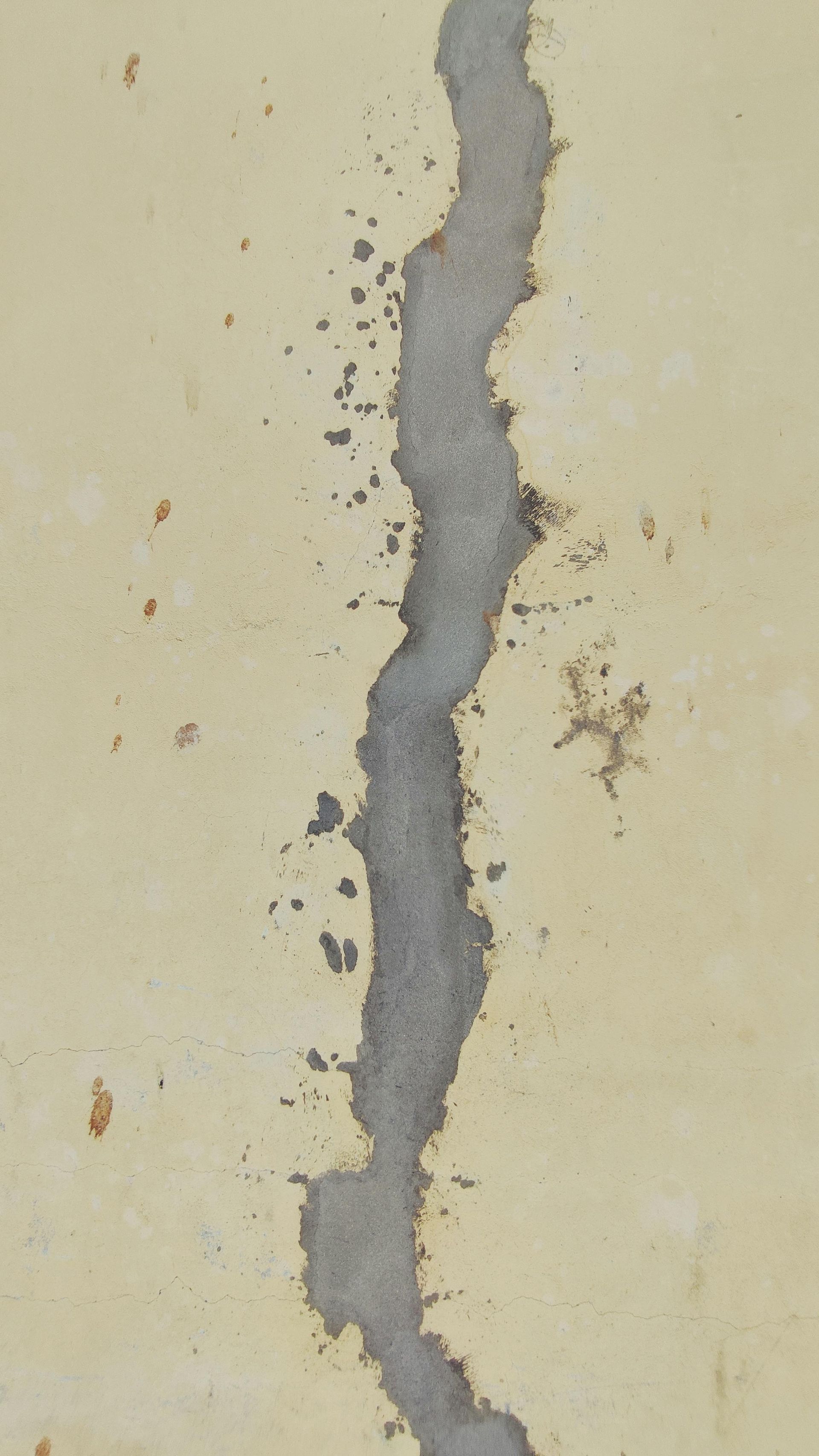 Vertical wall with a large, zig-zagging gray crack filled with cement. The wall is painted a faded yellow.