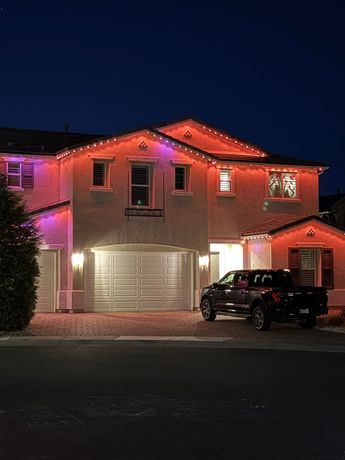 Two-story house glowing with red and purple lights at night, with a black SUV parked in the driveway