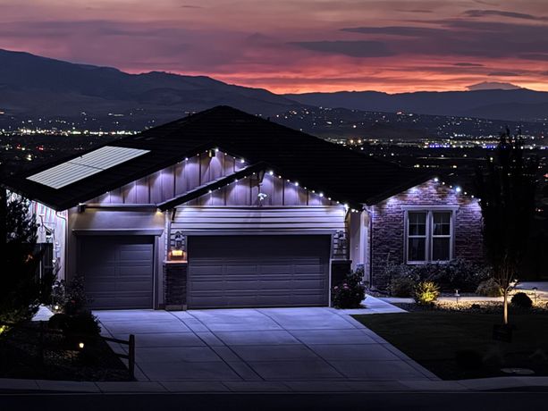 House and driveway lit at dusk with purple sky and mountain backdrop