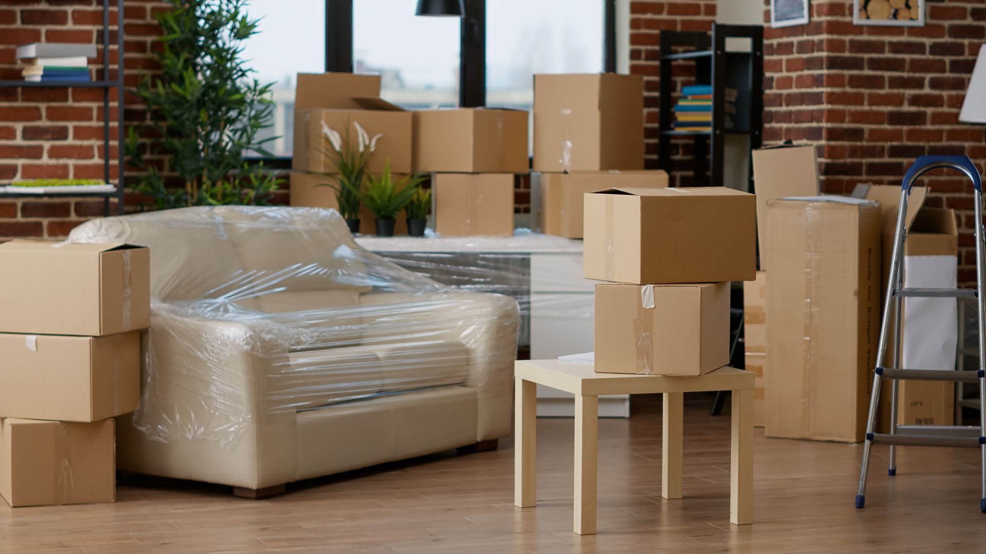 Des cartons et des meubles emballés dans du plastique dans une pièce, indiquant un déménagement ou une relocalisation.