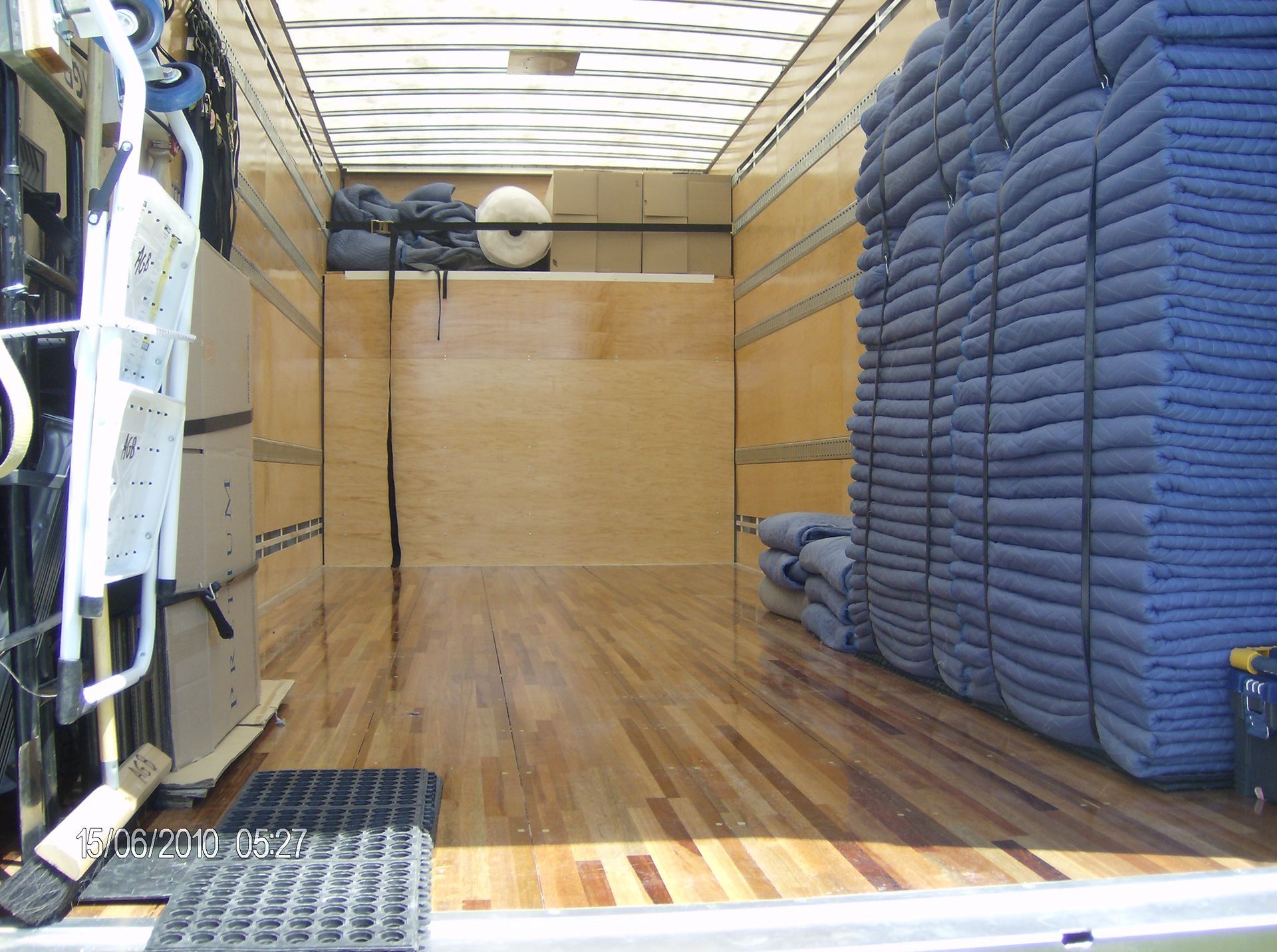 À l'intérieur d'un camion de déménagement, avec des piles de couvertures bleues, un plancher en bois et des cartons empilés.
