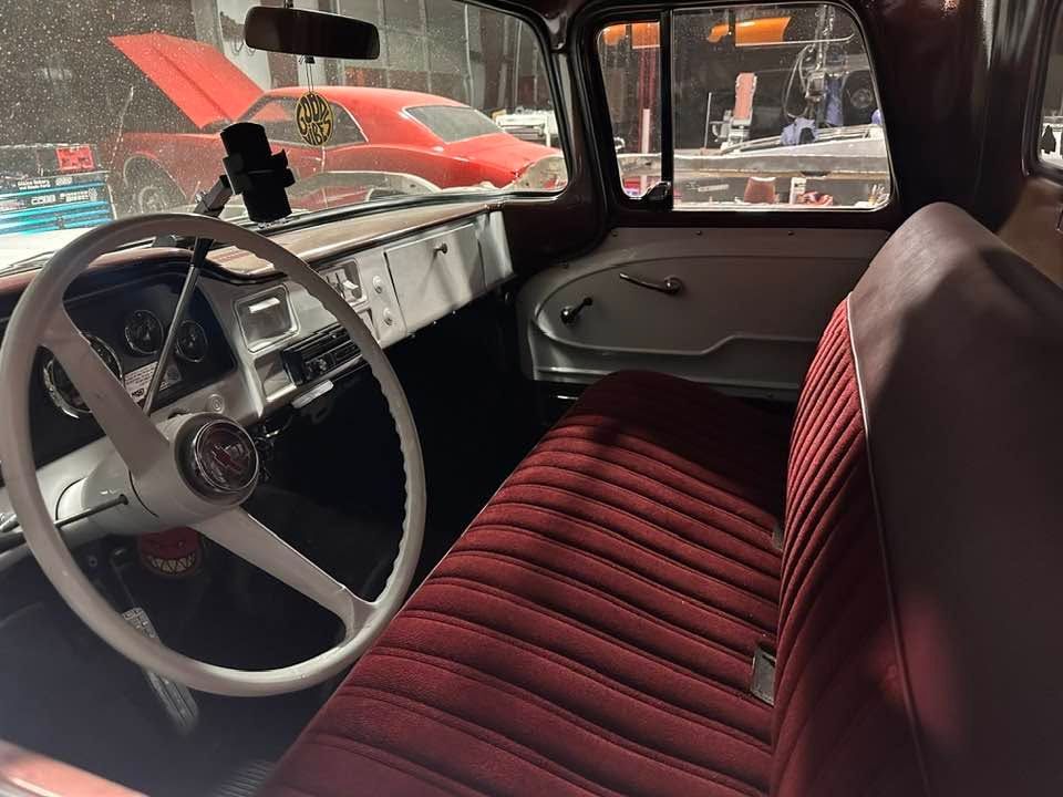 Vintage car interior with red bench seat, white steering wheel, and dashboard view through open window | Pro Veterans Automotive