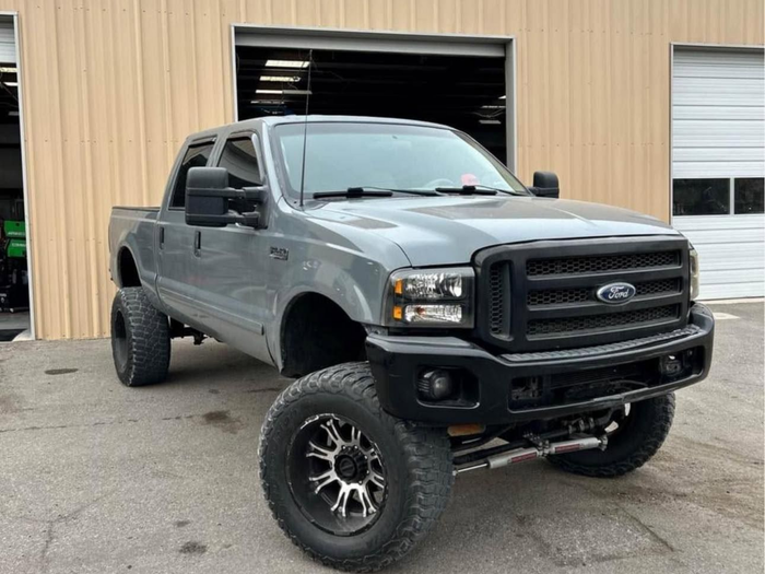 Gray lifted Ford pickup truck parked outside a beige garage, front three-quarter view