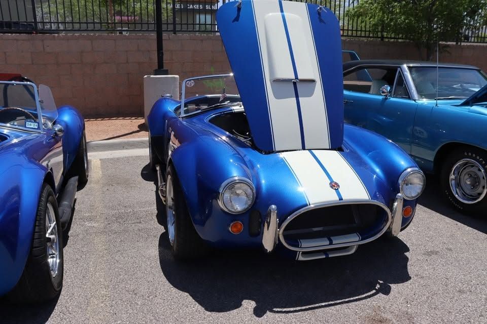 Blue vintage sports car with white racing stripes and raised hood at an outdoor car show | Pro Veterans Automotive
