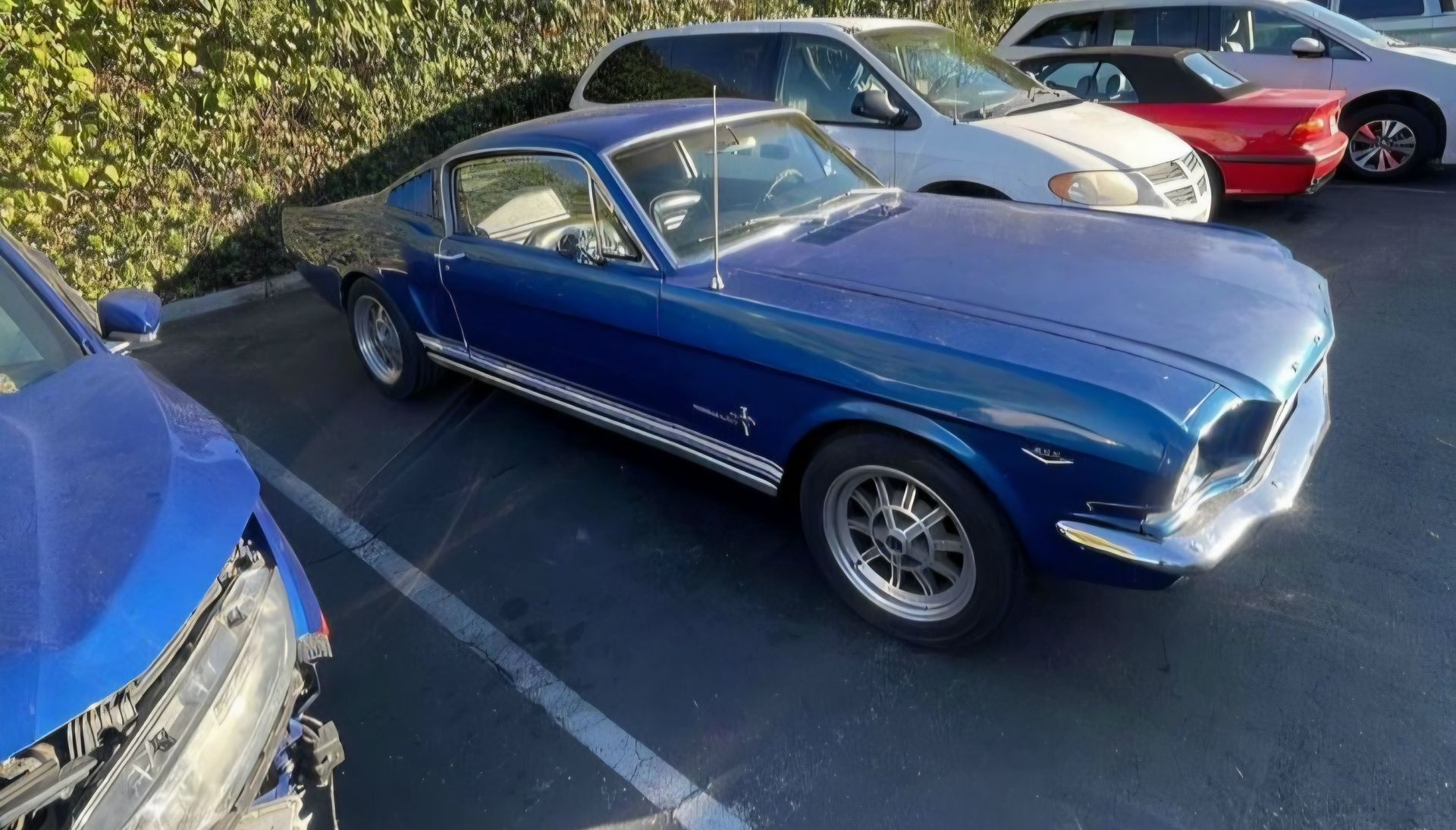 Blue classic Ford Mustang parked in a lot beside red and white cars, viewed from the front-left angle | Pro Veterans Automotive
