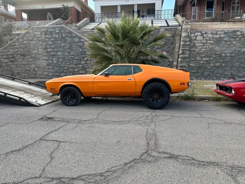 Orange classic car parked on a street beside a red car, with stone walls and houses behind | Pro Veterans Automotive