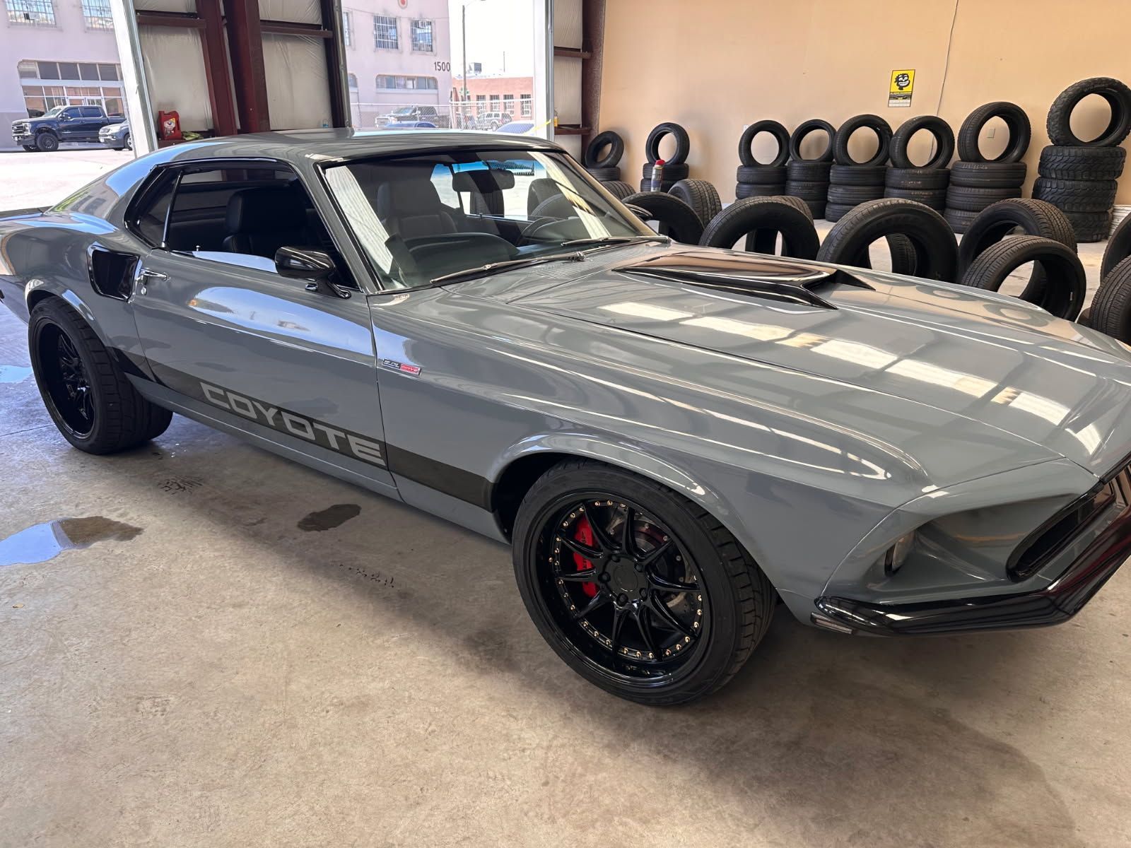 Gray classic muscle car parked indoors beside stacks of tires. | Pro Veterans Automotive