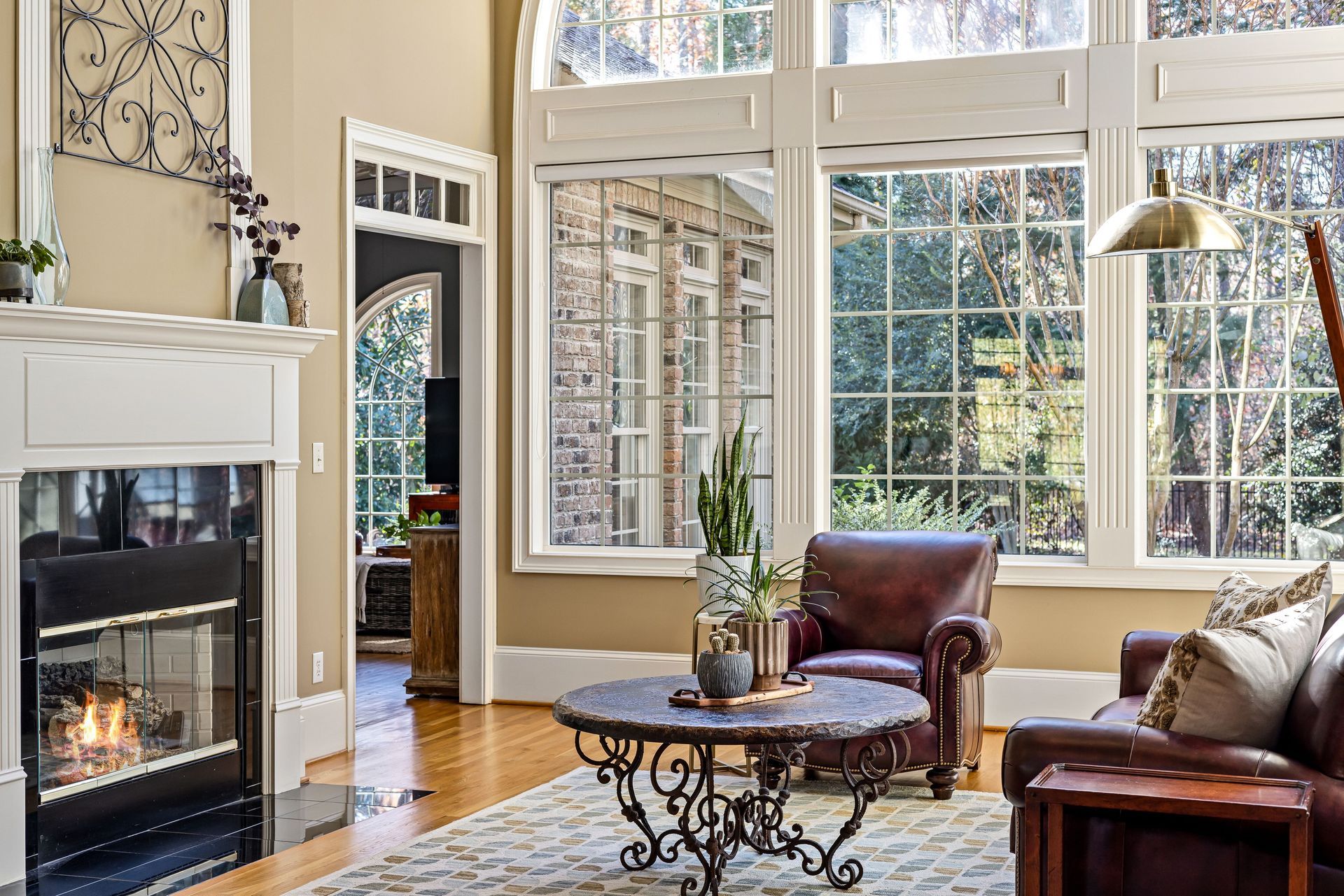 Bright living room with a fireplace, large windows, leather chairs, and a round coffee table