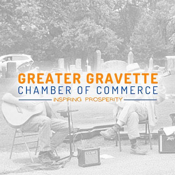 Two people play acoustic guitars outside, overlaid with the Greater Gravette Chamber of Commerce text and logo.