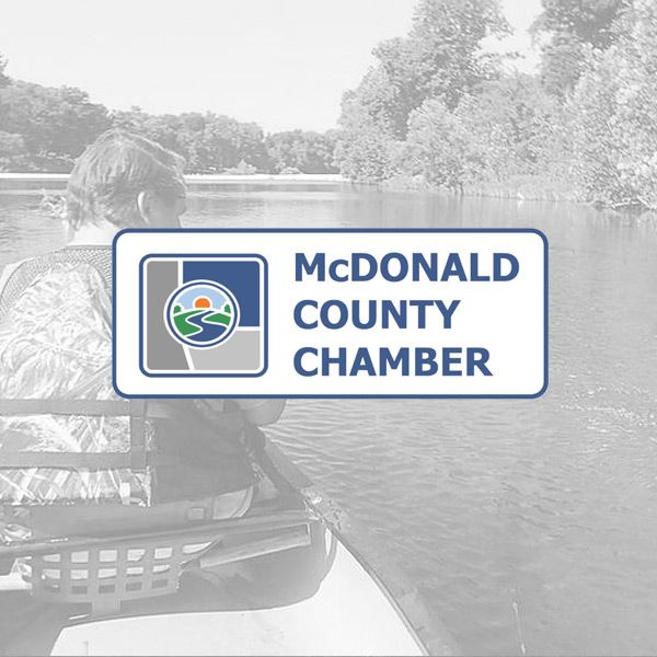 Logo for the McDonald County Chamber featuring a river landscape, overlaid on a faded background of someone in a canoe.