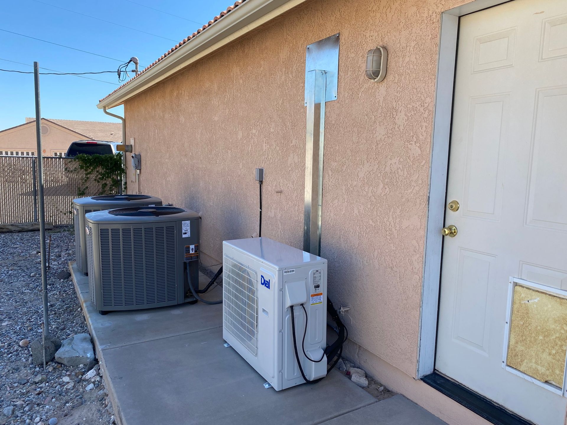Two air conditioners are sitting on the side of a house next to a door.