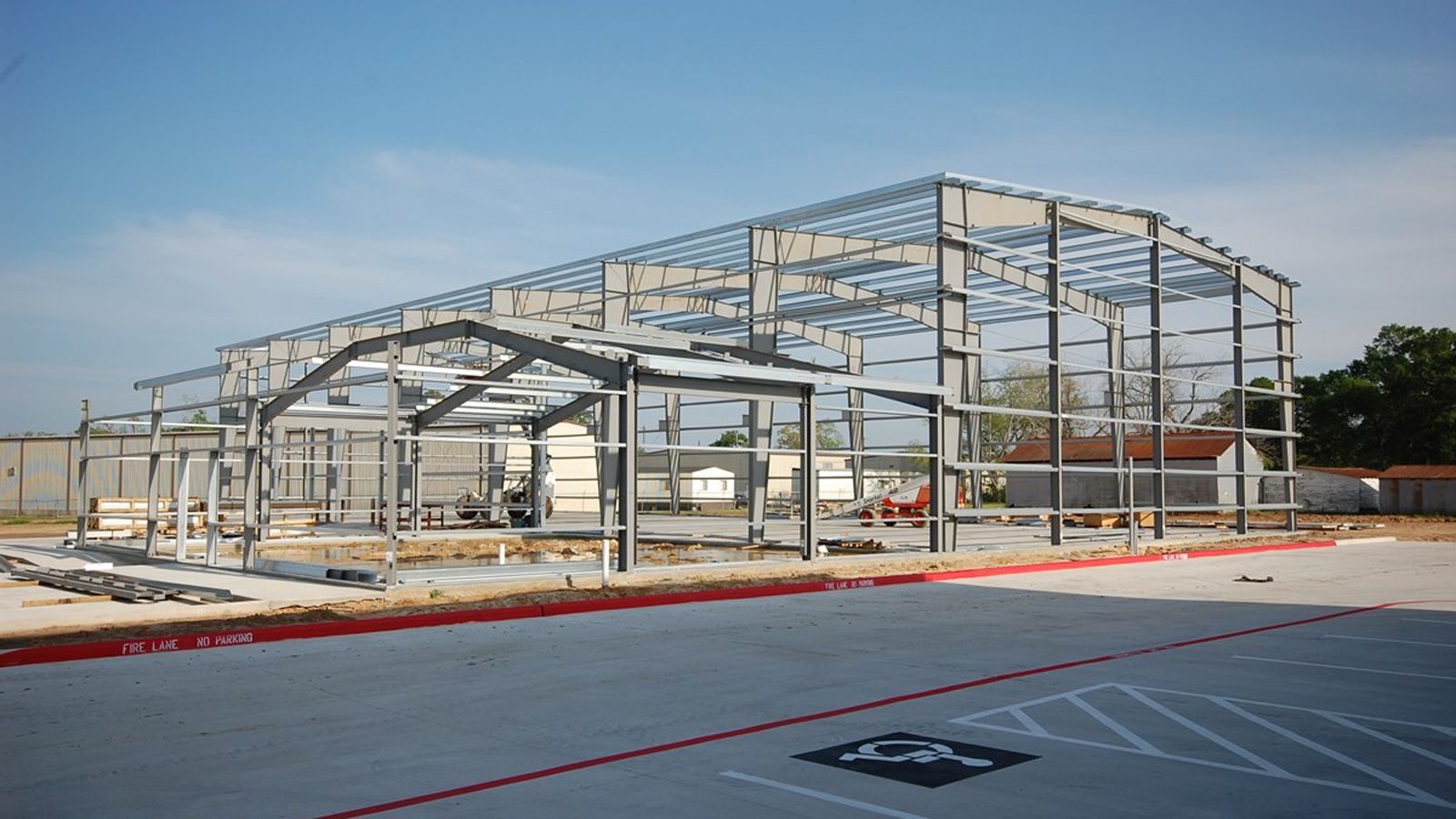 Steel framework of a large building under construction, on a concrete slab, with a clear sky.