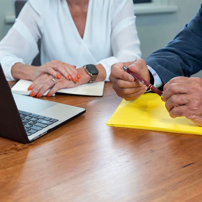 Two people reviewing documents at a wooden table with a laptop and yellow folder